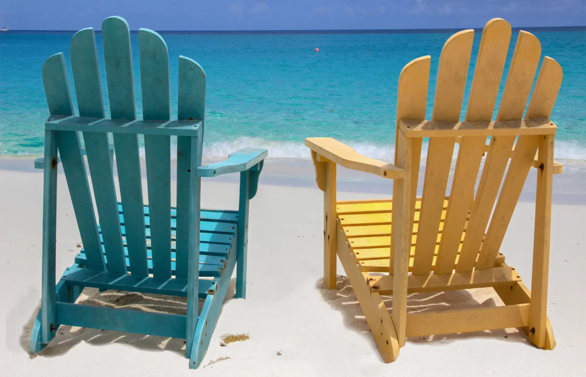 Two colorful chairs on a sandy beach facing the ocean.