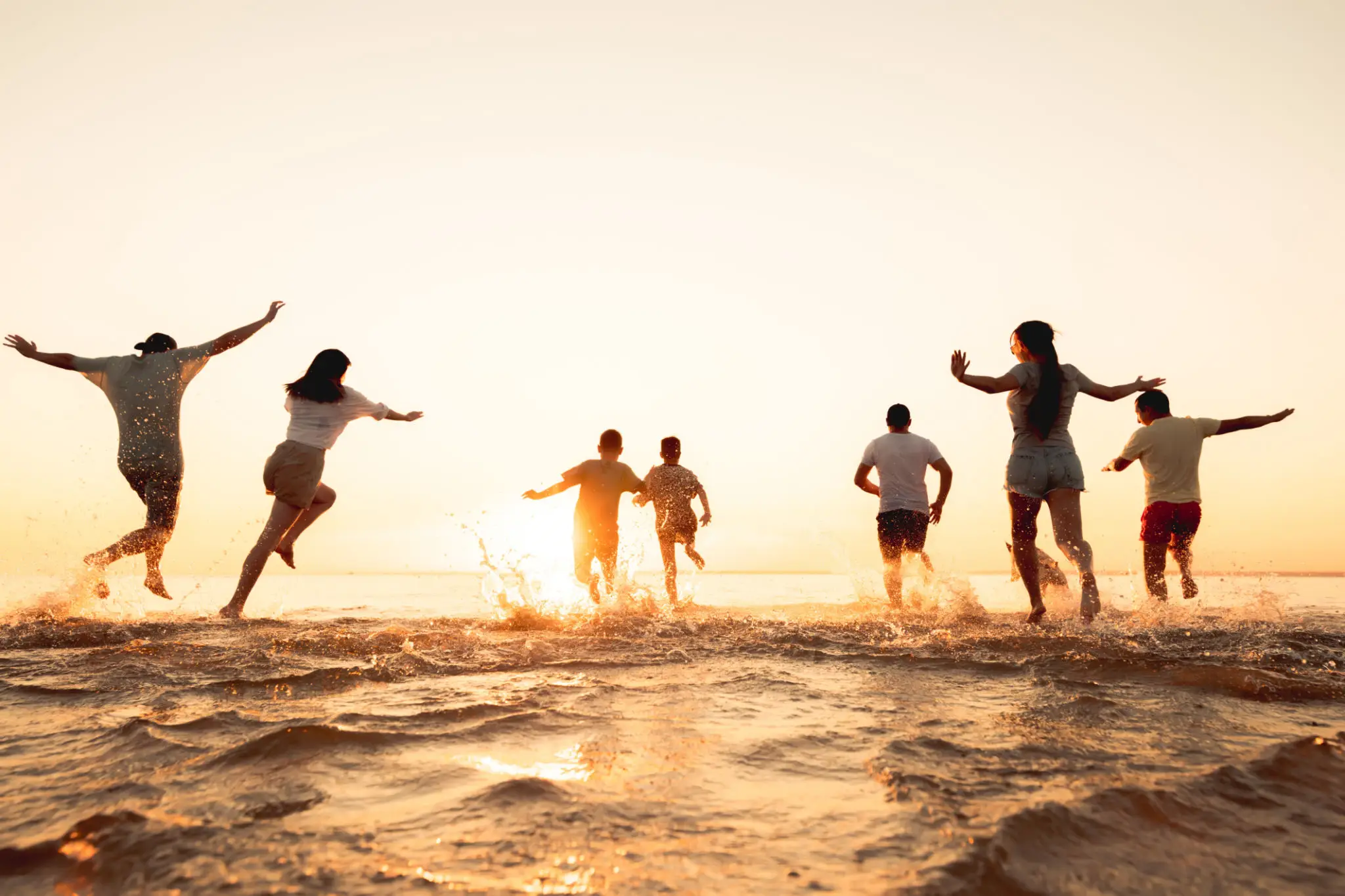 People running and playing on the beach at sunset.