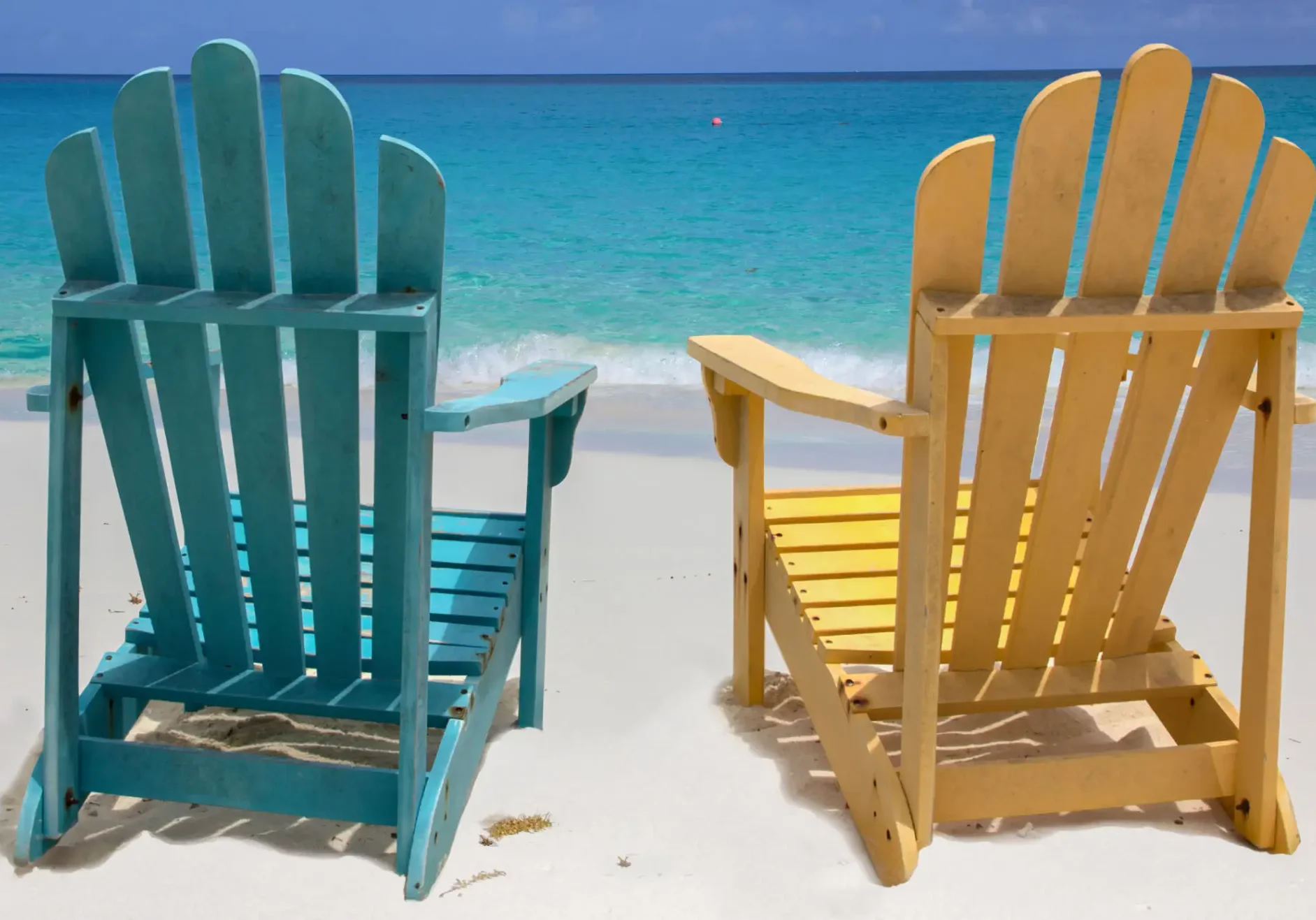 Two colorful chairs on a sandy beach facing the ocean.