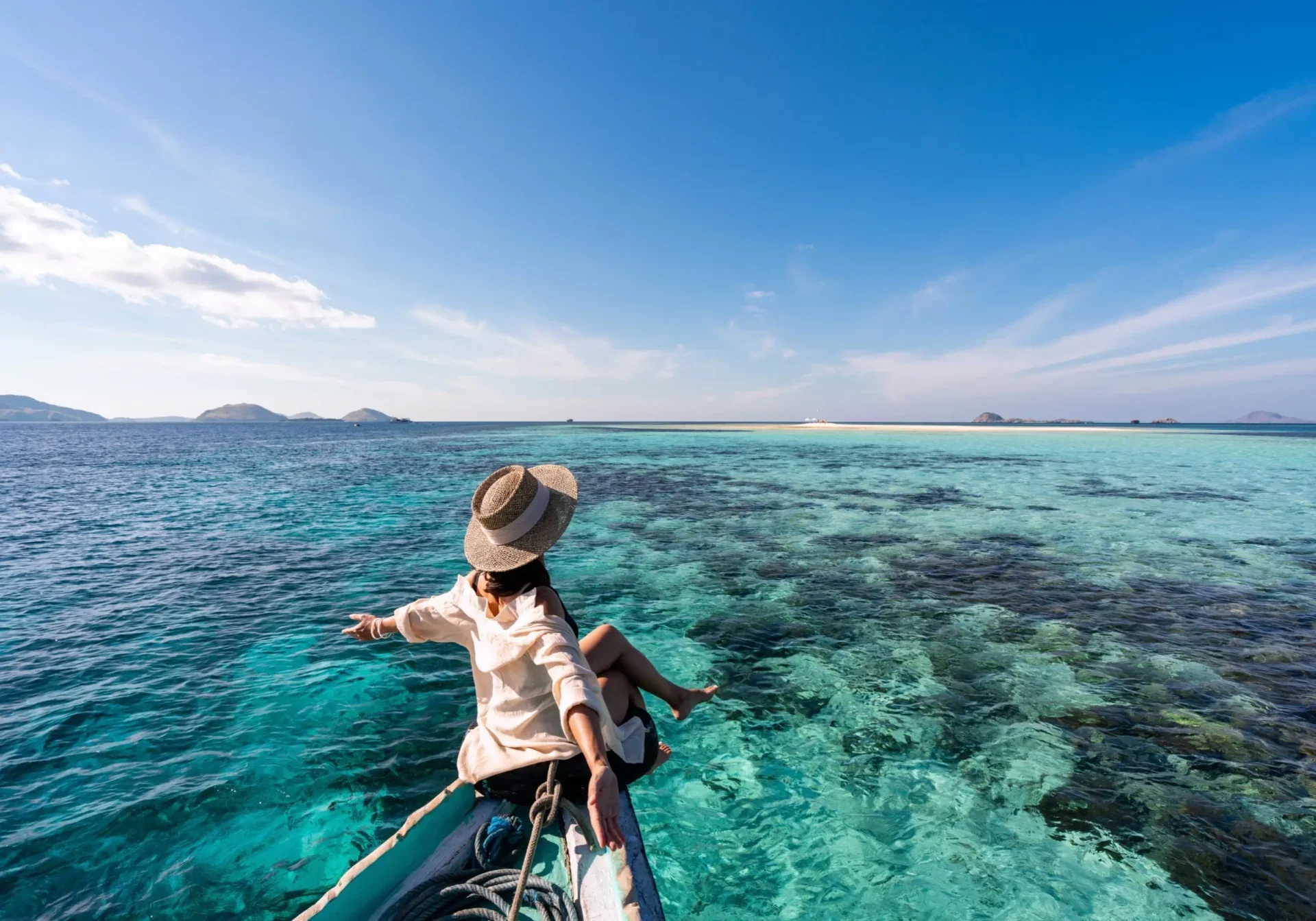 Person in a hat on a boat overlooking clear blue ocean water.
